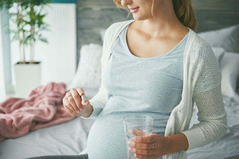 Madre gestante tomando suplementos nutricionales para embarazadas con un vaso de agua